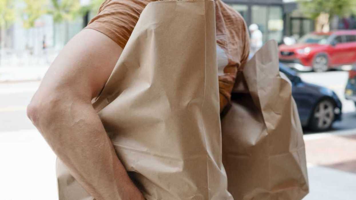 Close-up of an unrecognizable man walking down the street carrying bags of groceries.
