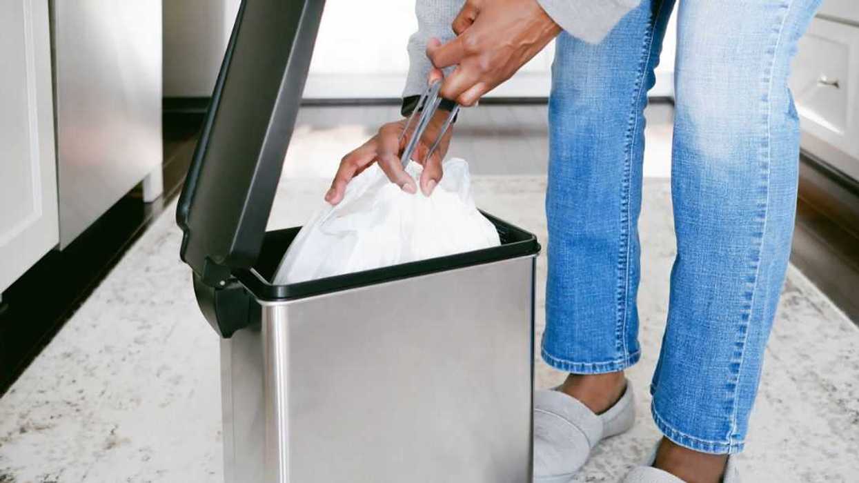Close-up of an unrecognizable woman removing kitchen trash bag from can.