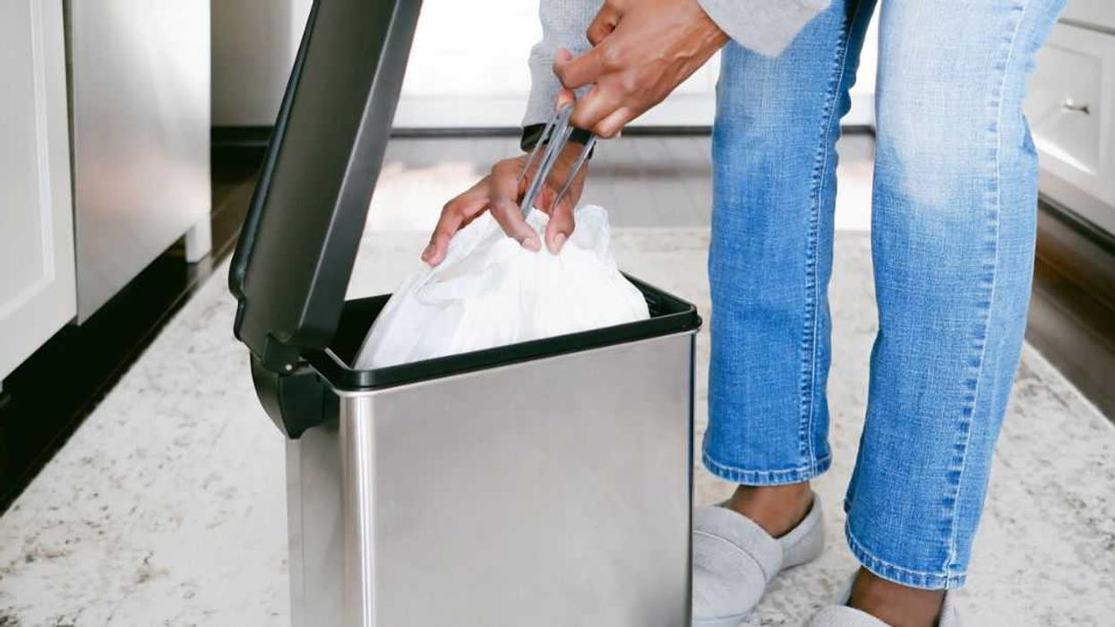 Close-up of an unrecognizable woman removing kitchen trash bag from can.