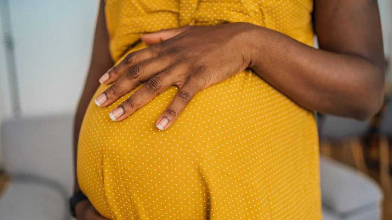 Close-up of pregnant woman in yellow dress embracing her pregnant belly.