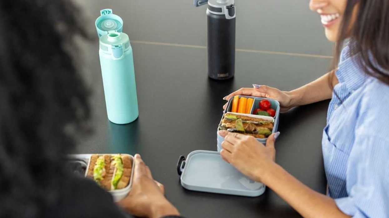 Close-up of two woman coworkers sitting at desk with lunch boxes in office. Healthy food in lunch boxes for female colleagues at work desk.