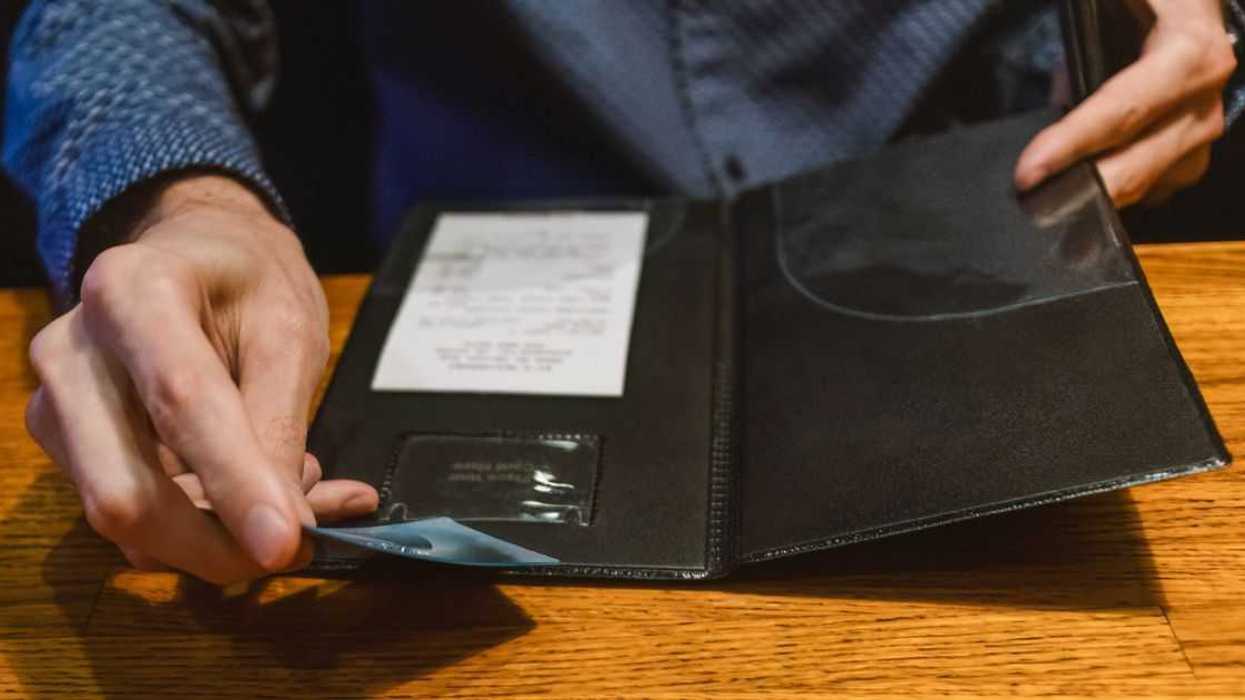 Close-up of unrecognizable man holding credit card while reviewing bill at restaurant