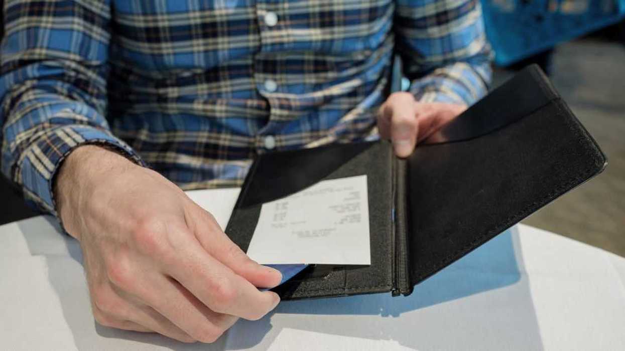 Close-up of unrecognizable man reviewing check at restaurant while placing credit card in holder.