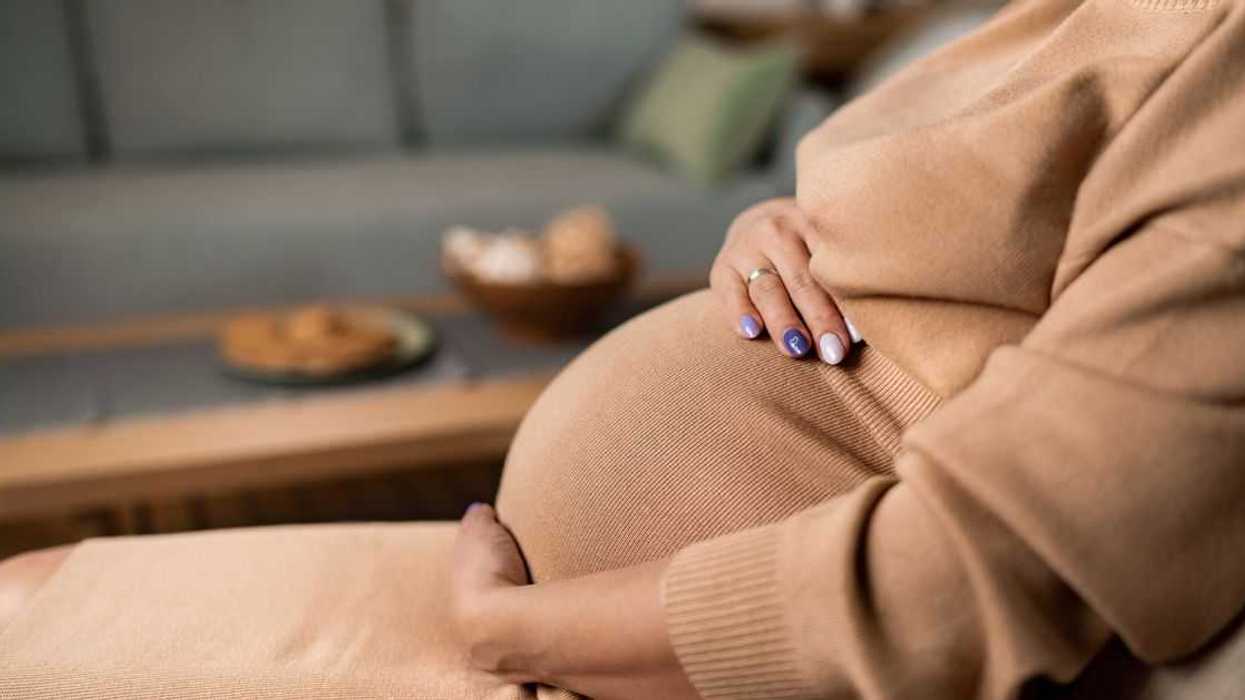 Close-up of unrecognizable pregnant woman touching her belly while sitting at home.