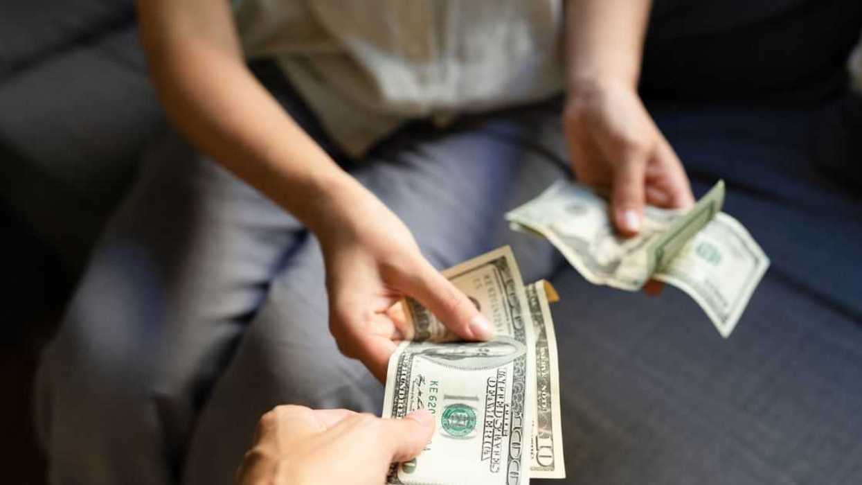 Close-up of woman taking US dollar banknotes from another woman.