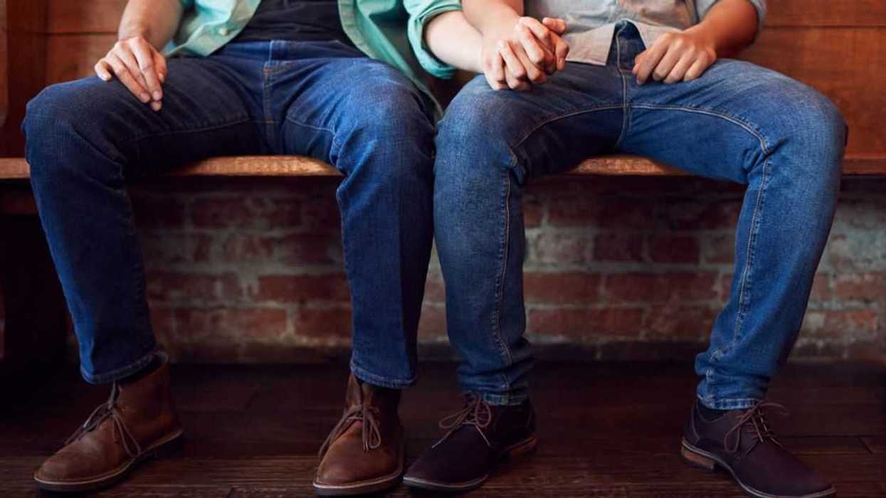 Close Up On the Feet Of a Same Sex Male Couple Holding Hands while Sitting On a Bench Together.