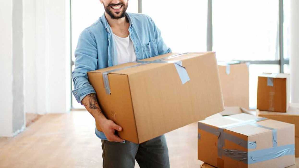Closeup front view of a smiling young man carrying boxes as he moves into his new apartment.