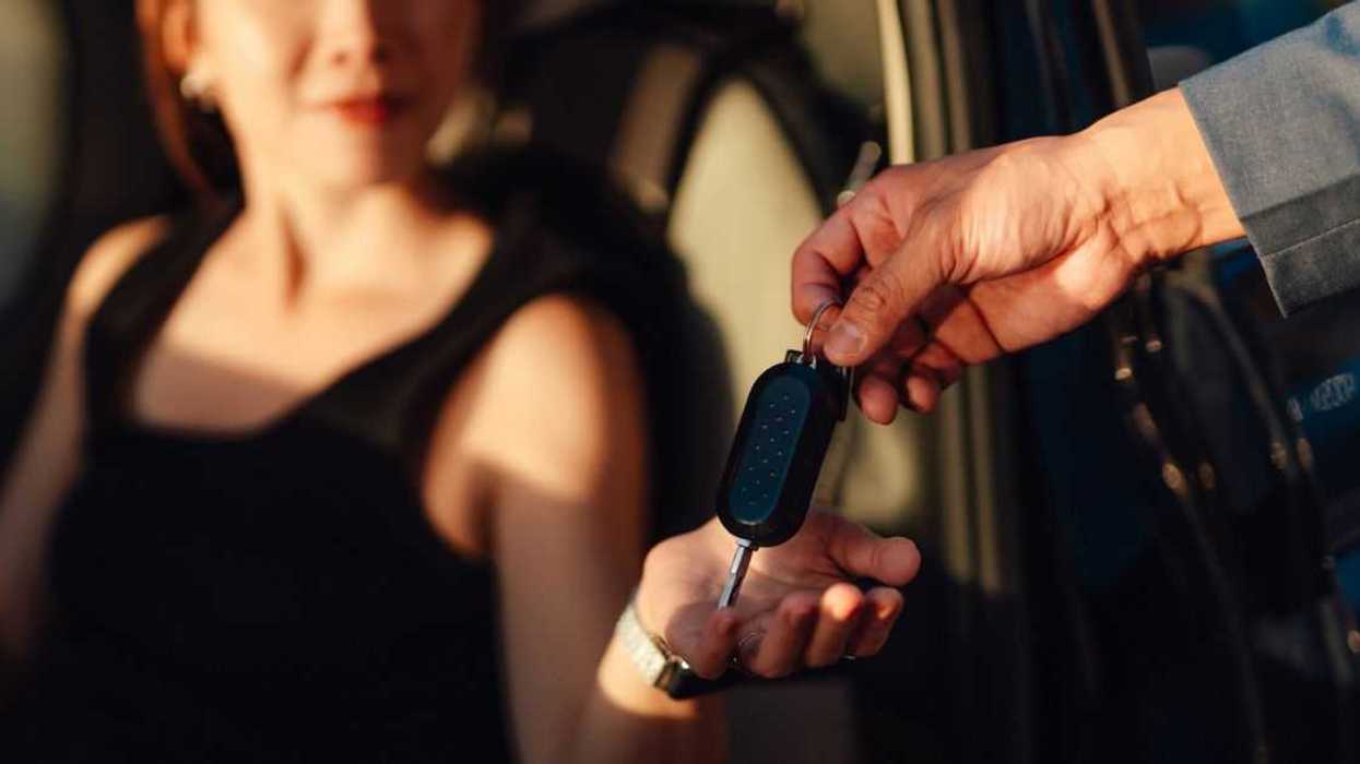 Closeup of a young woman receiving car keys from a sales representative showcasing automotive transactions or rental services in a covered parking environment.
