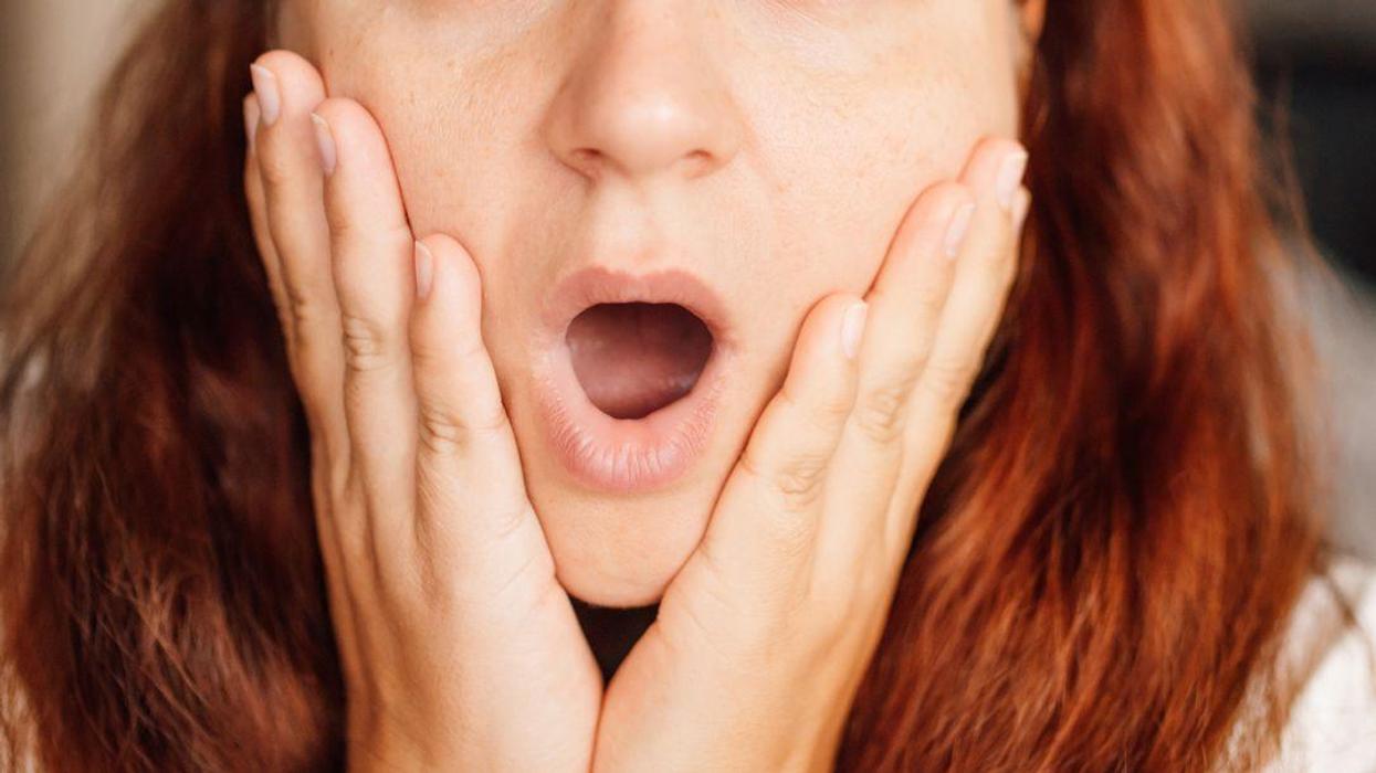 Compelling portrait of charming mature lady with red hair, with hands pressed to sides of face, eyes wide with astonishment, and mouth open, as if she just received shocking news.