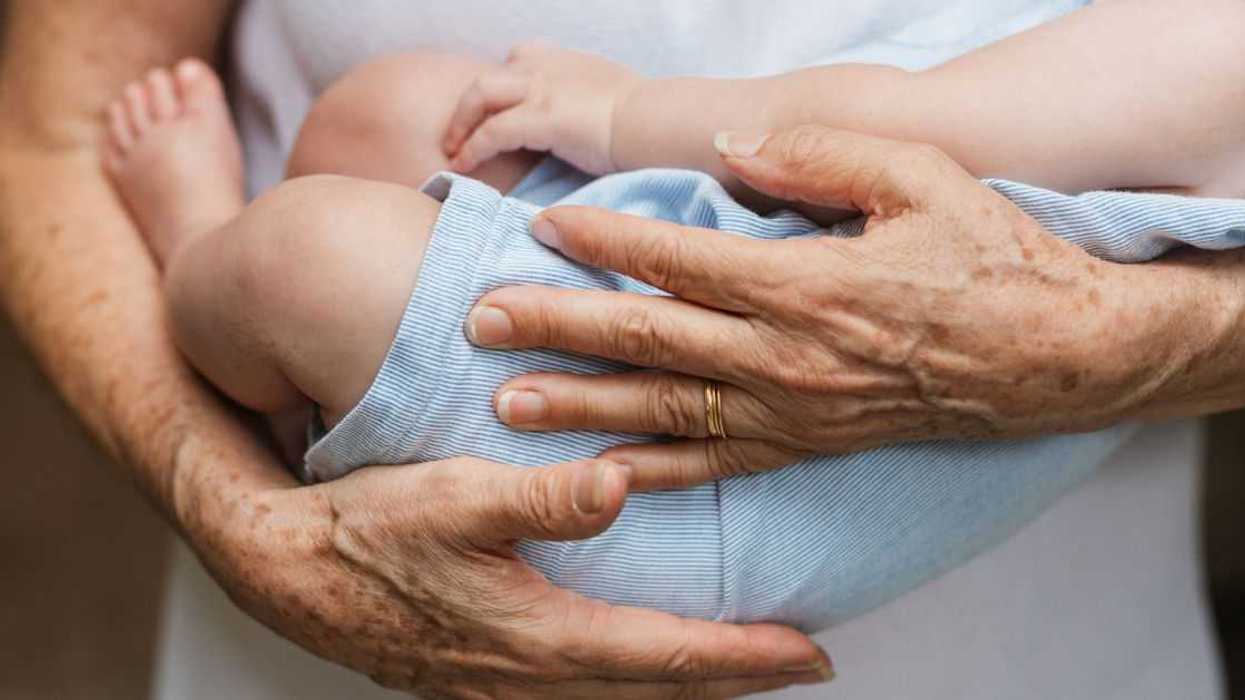 Cropped close-up photo of a baby boy sleeping in arms of a person.