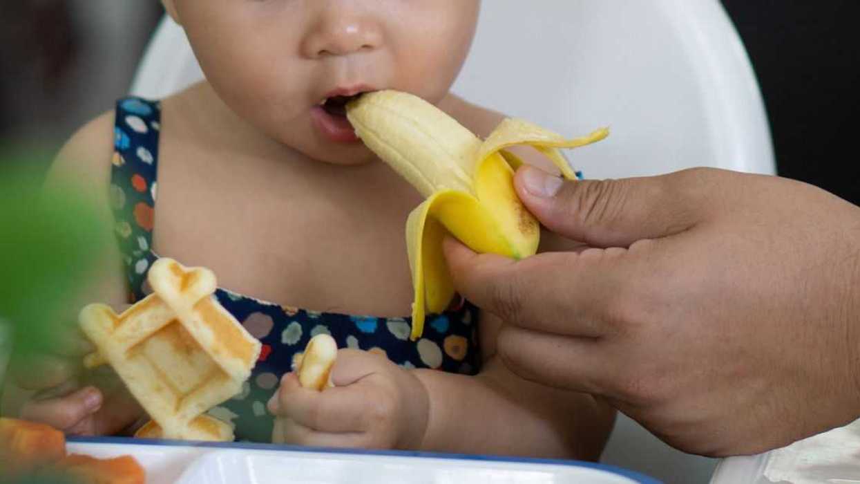 Cropped Hand Of a Mother Feeding Banana To her Daughter In a Restaurant.