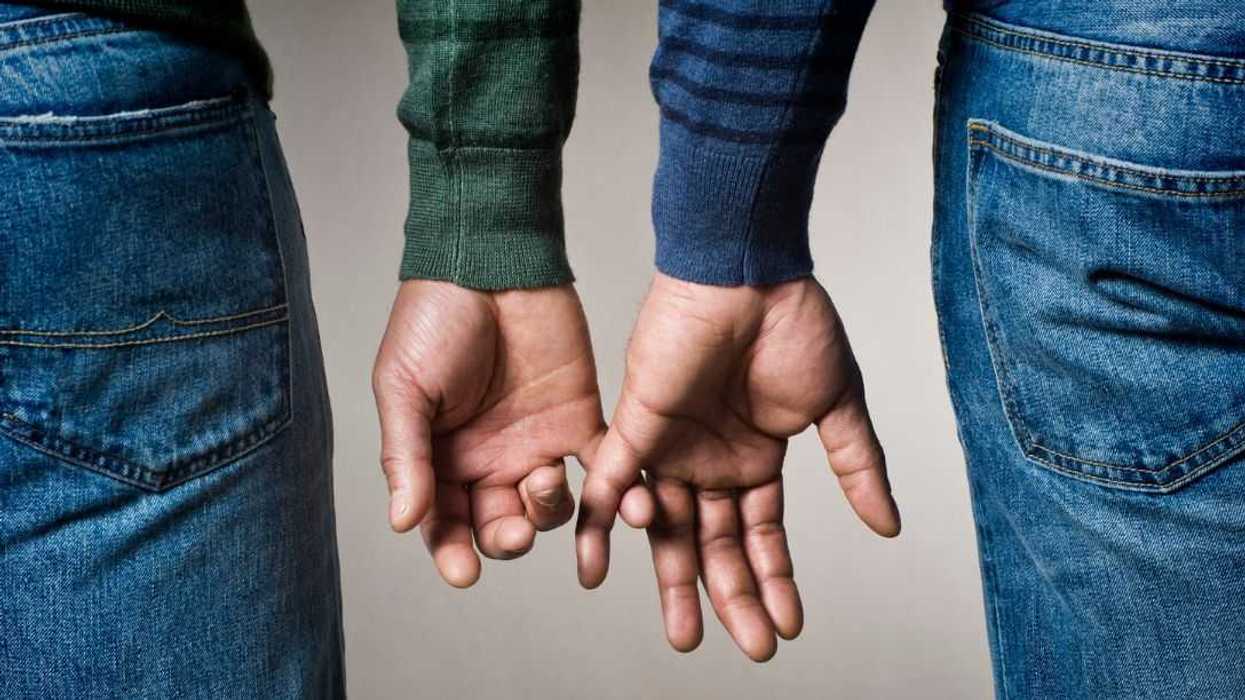 Cropped photo of a same sex, male couple about to intertwine their fingers.