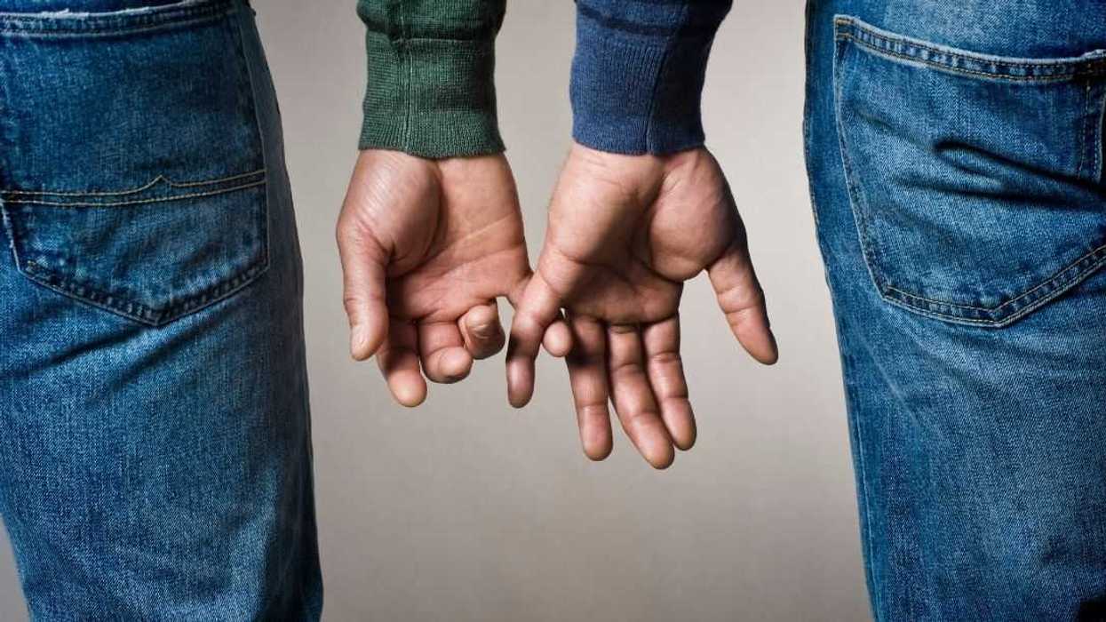 Cropped photo of a same sex, male couple about to intertwine their fingers.