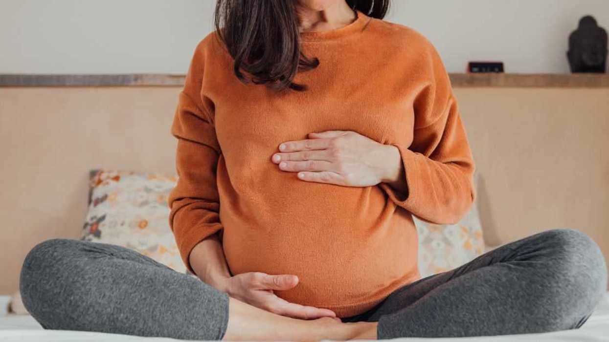 Cropped Pregnant woman, sitting in crossed legs in be at home holding her belly