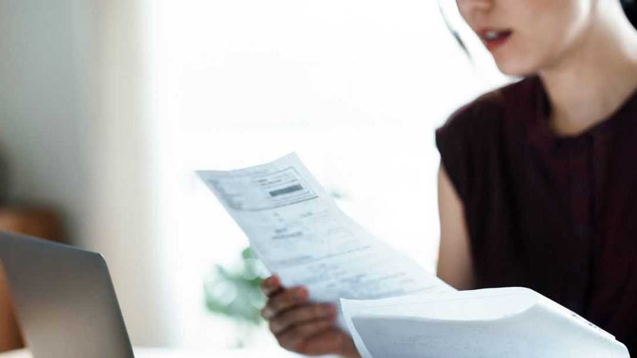 Cropped shot of a woman sitting at dining table, handling personal finance with laptop. She is making financial plan and planning budget as she go through her financial bills, tax and expenses at home. Wealth management, banking and finance concept