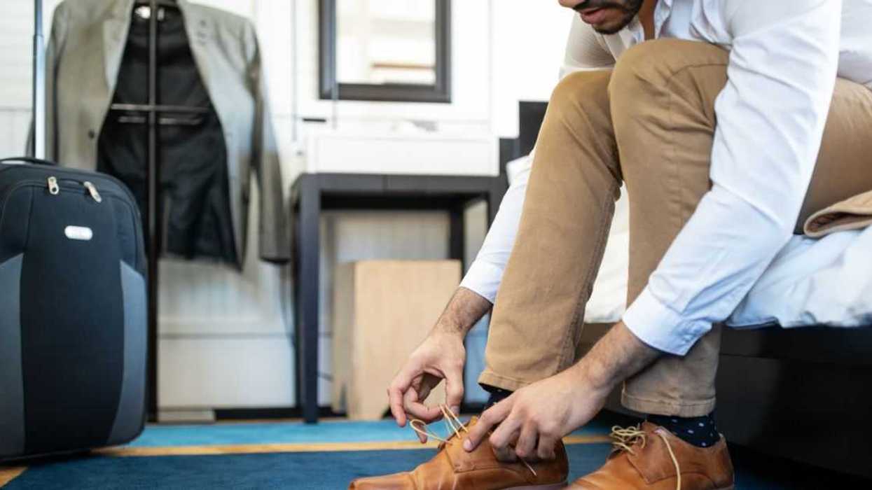 Cropped shot of man removing his shoe while sitting on hotel bed.