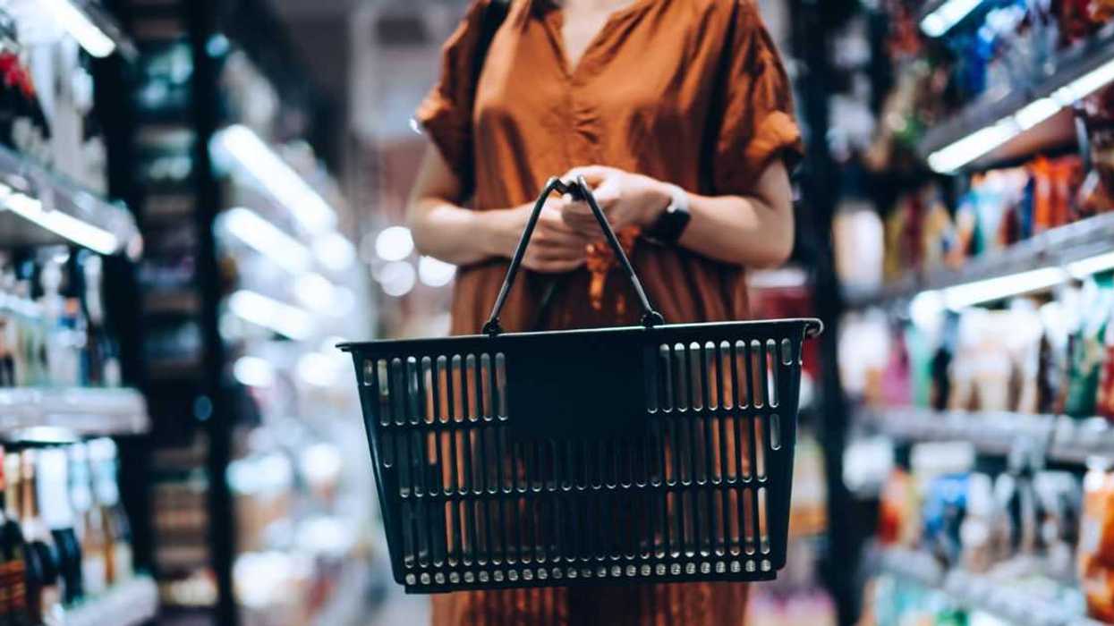 Cropped shot of young woman carrying a shopping basket, standing along the product aisle