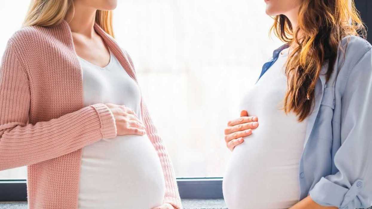 Cropped view of smiling pregnant women standing by window.