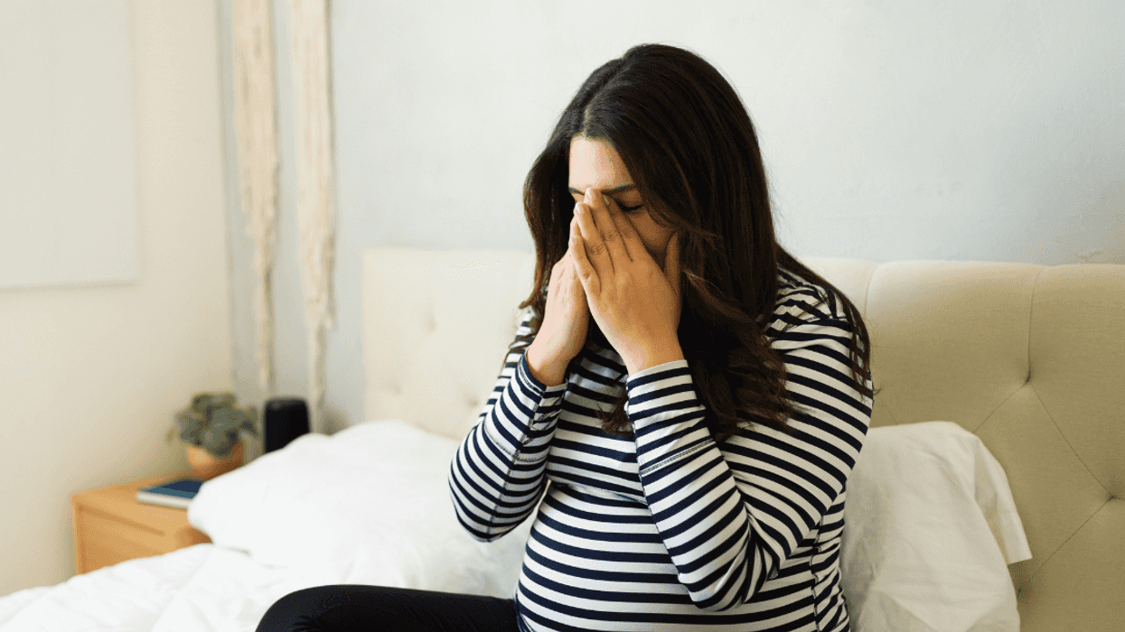 crying pregnant woman seated on bed