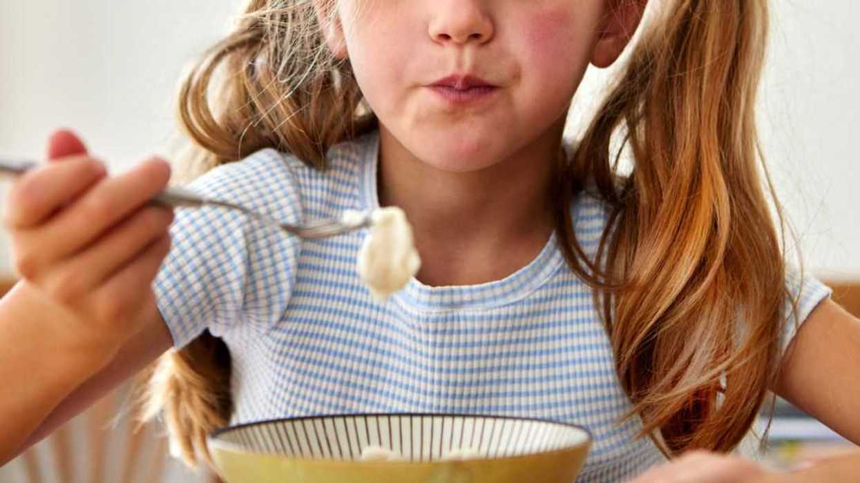 Cute girl eating yogurt or ice cream from a bowl at home.