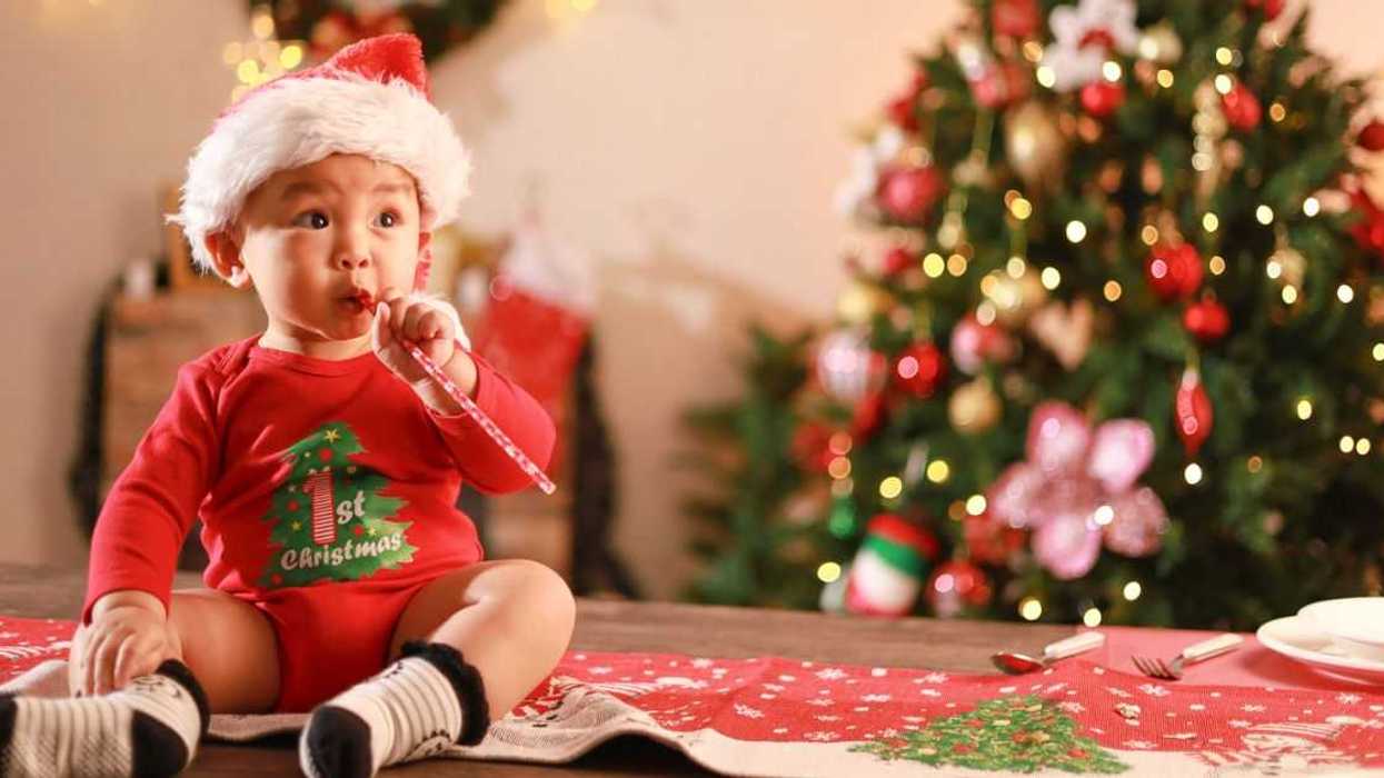 Cute little boy wearing Santa hat sitting on table, playing with toys on Christmas day and Christmas tree background.