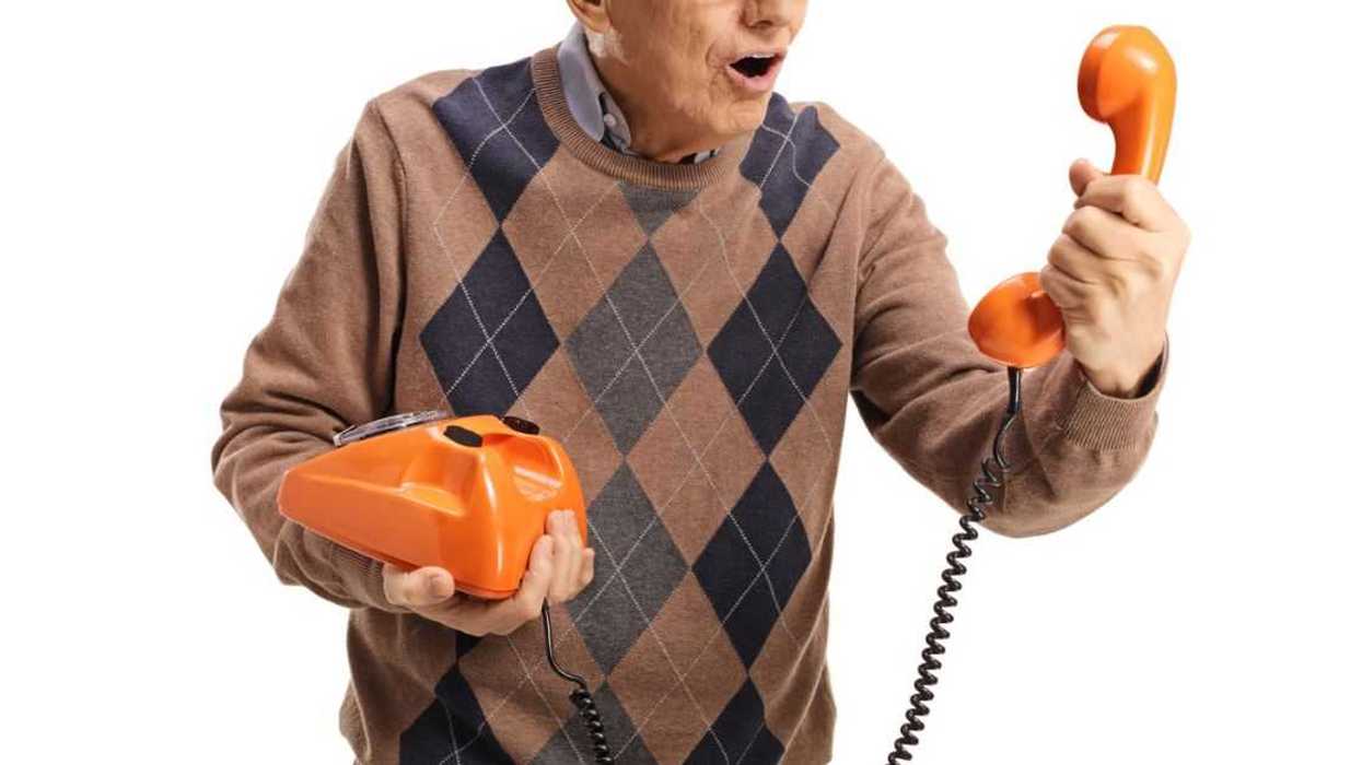 Elderly man holding an old vintage rotary phone and looking at the handset isolated on white background.