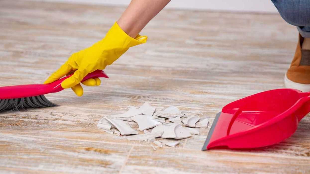 Faceless person clean up a broken plate with broom and dustpan.