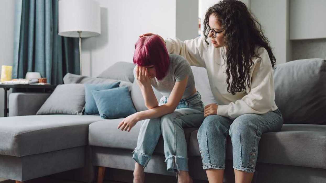 Feeling lonely and vulnerable. Teenage girl covering her face and crying on a couch, while her mother strokes her hair.