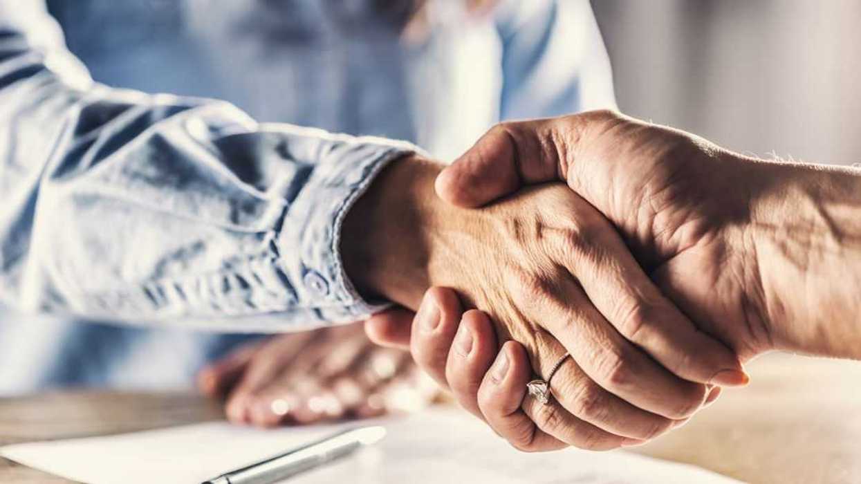 Female and male shake hands over a closed deal signed by a pen on a paper below.