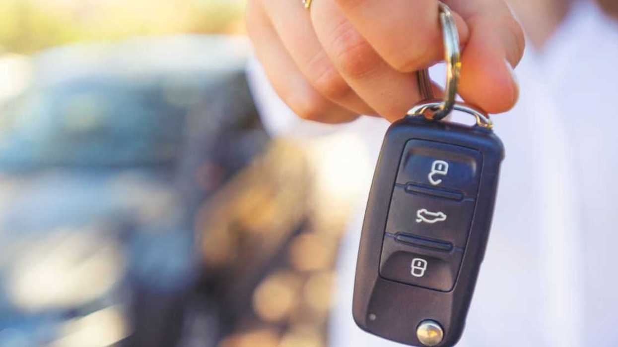 Female car salesperson handing over the new car keys. There is a new car behind her out of focus. Close up with Copy space.