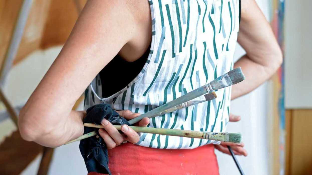 Female painter in her atelier, holding paintbrushes in her hand.