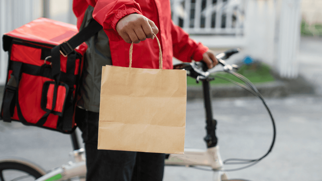 food in paper bag being delivered by person in red jacket on a bicycle