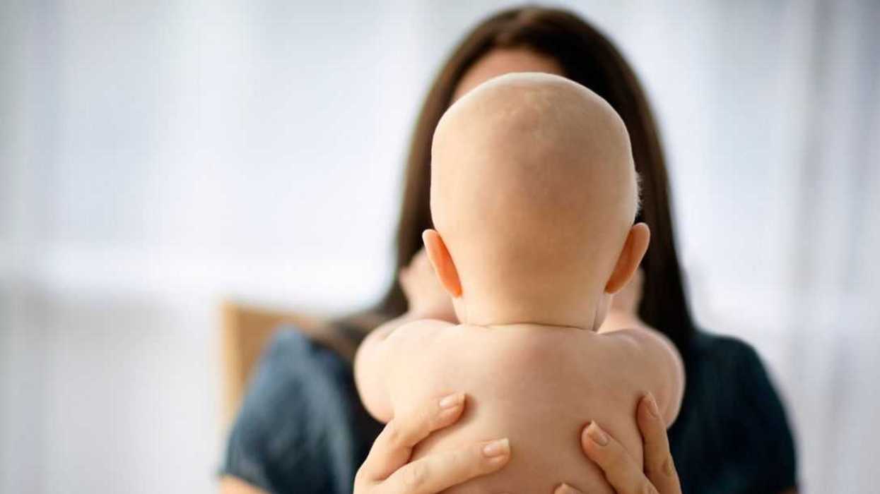 From the perspective behind the baby, mother holds him up to the camera. We see neither face, but the hands of the woman and baby appears to be touching her face.