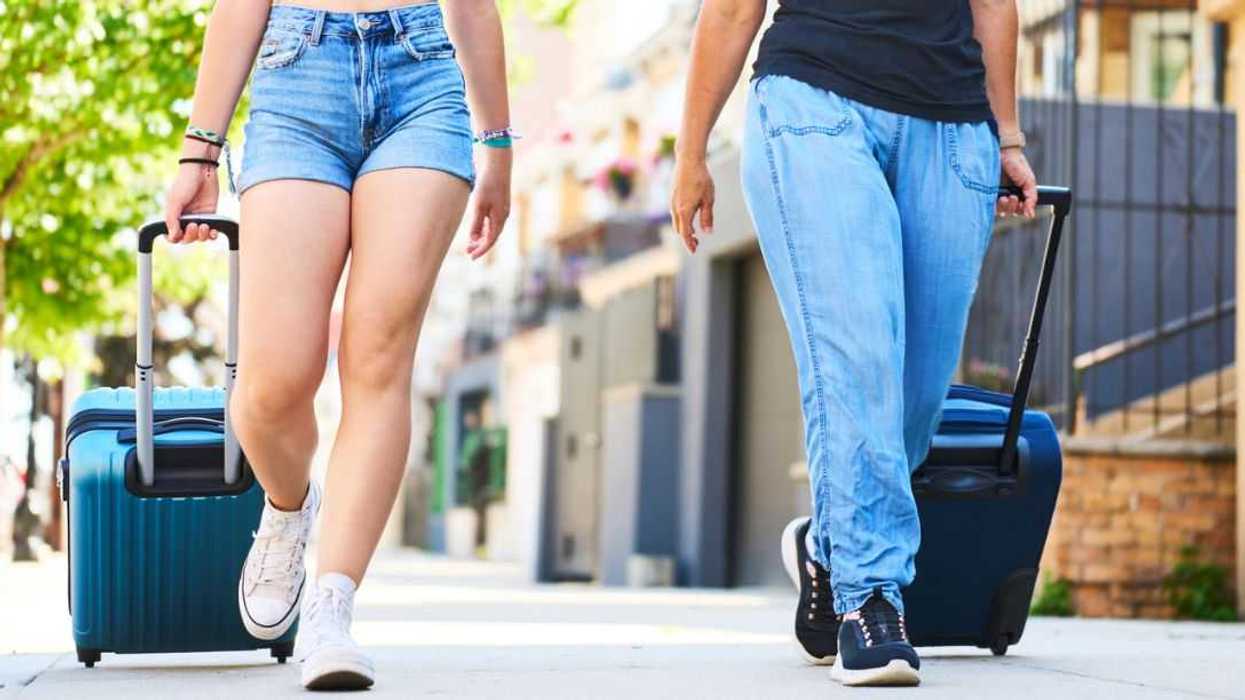 Front view of the legs of a young woman in shorts and her mother in jeans walking on the sidewalk on the street with US flags on the outside of the houses.