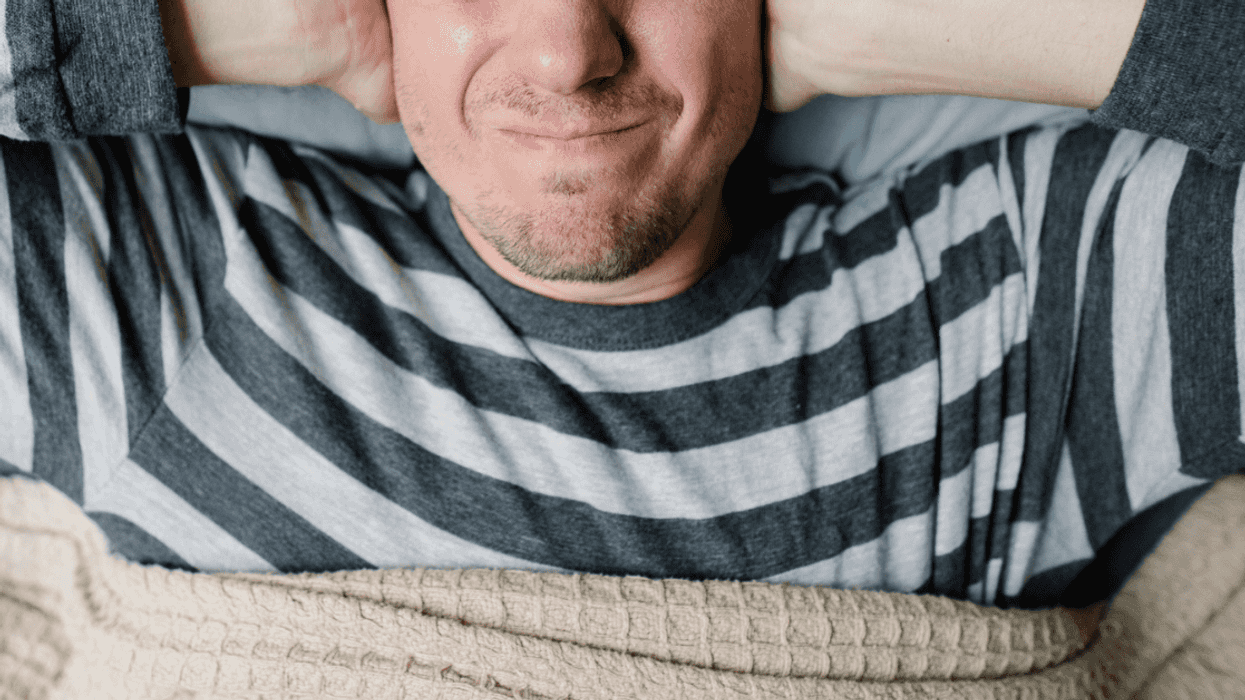 Frustrated man covering his ears while trying to go to sleep