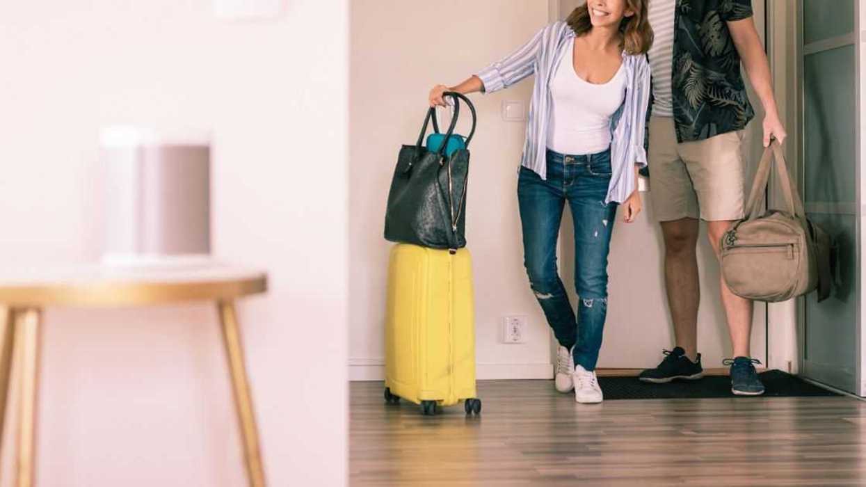 Full length pic of a couple with luggage looking around in an apartment while standing at doorway.