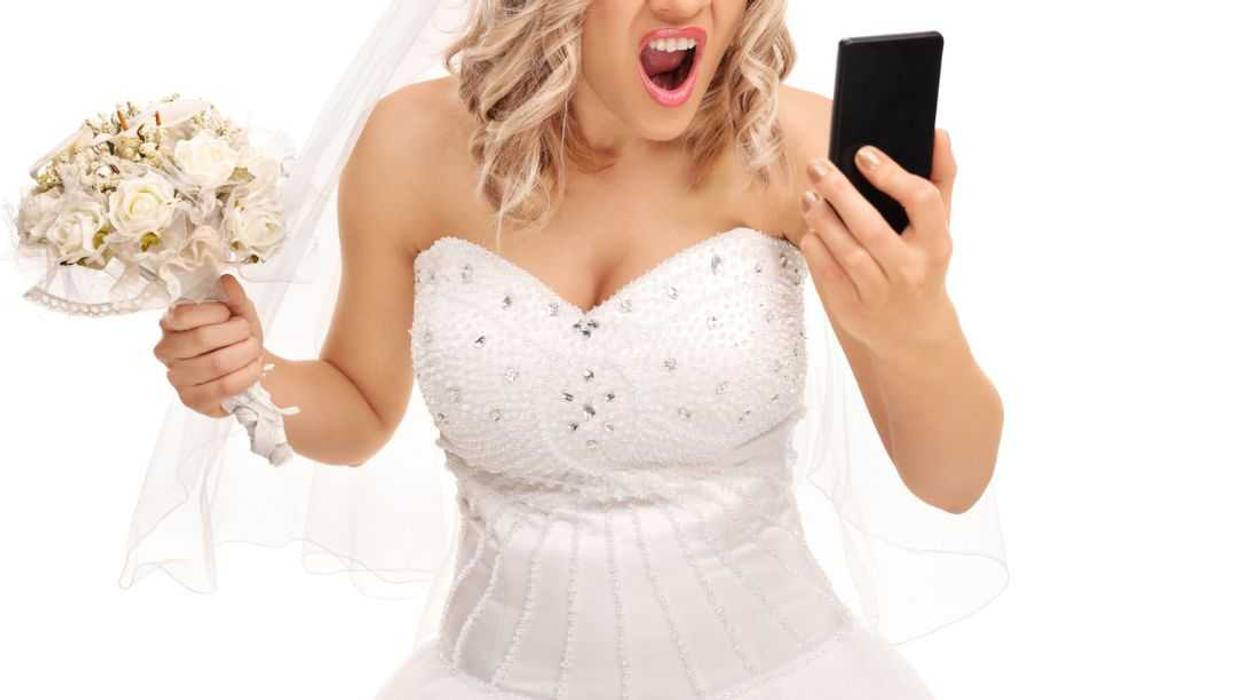 Furious young bride looking at her cell phone and screaming isolated on white background.