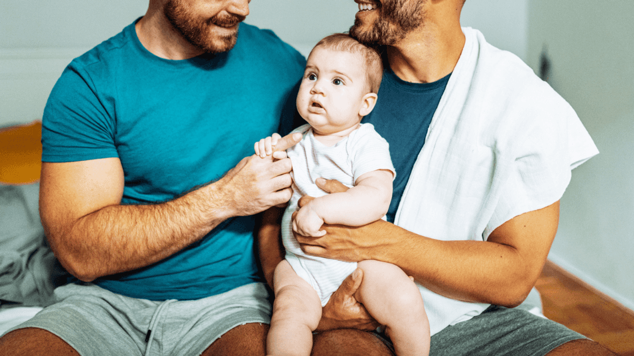 gay couple hold their baby while seated on a bed