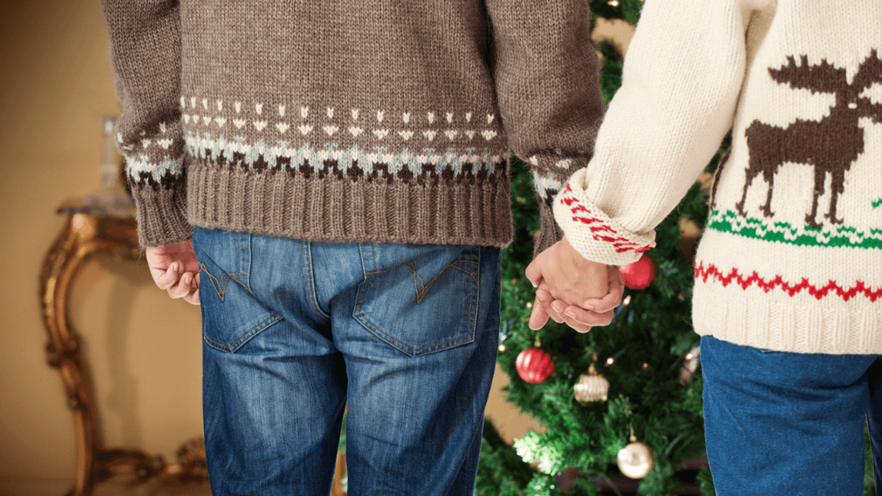Gay couple holding hands wearing Christmas sweaters.