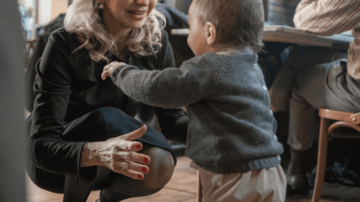 Granda crouching down and reaching for toddler.