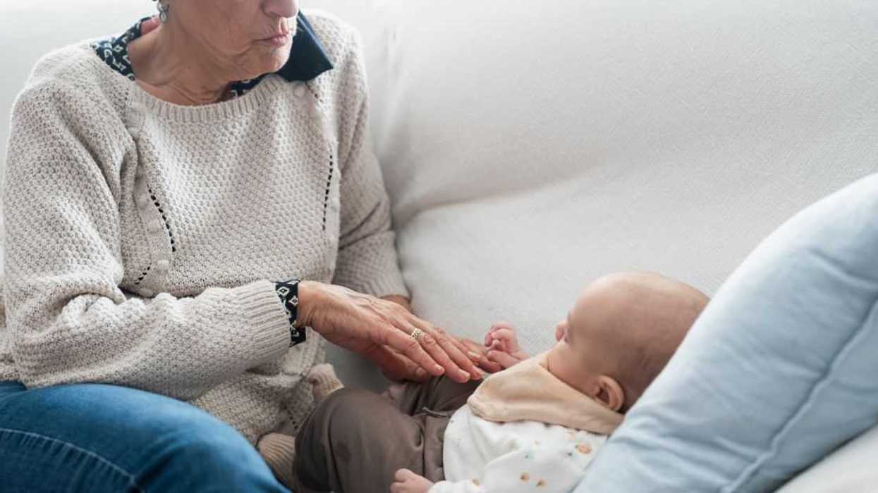 Grandmother caressing her newborn grandchild on the sofa: intergenerational connection and tender family moments.
