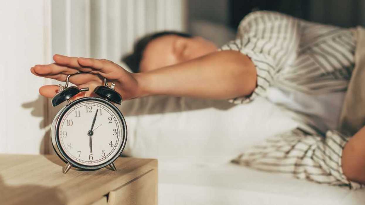 Hand of woman turning off alarm clock on night table.