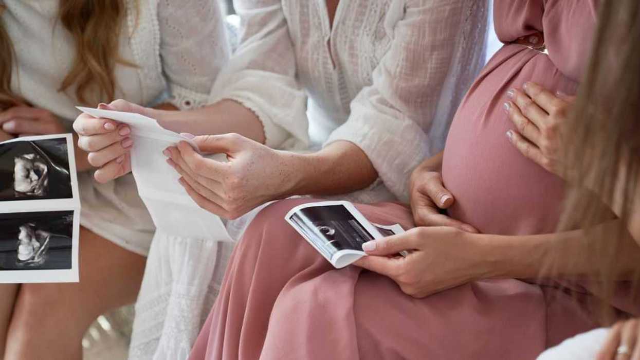Hands of pregnant woman with friends holding ultrasound scan result at baby shower.