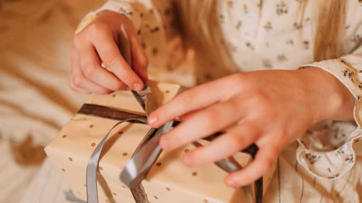 Hands untying a ribbon on a polka dot gift box.