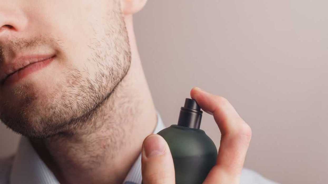 Handsome unshaven man applying perfume on neck, closeup. Space for text.
