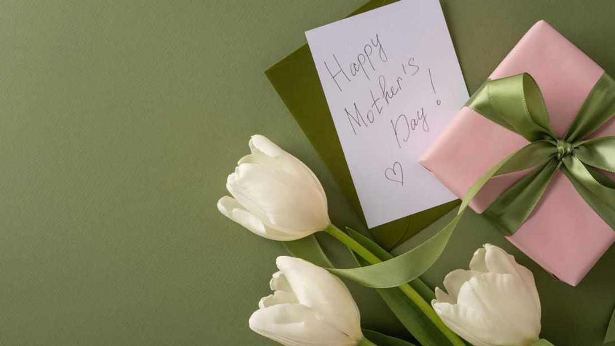Happy Mother's Day arrangement with a pink wrapped gift, white tulip stem and a handwritten card on a textured green background suggesting spring warmth and heartfelt appreciation.