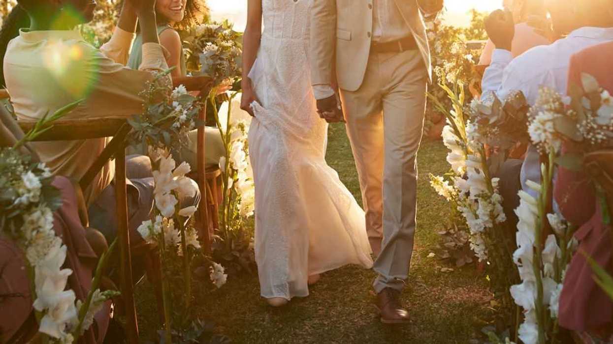 Happy young just married couple walking aisle amidst wedding guests during ceremony at sunset.