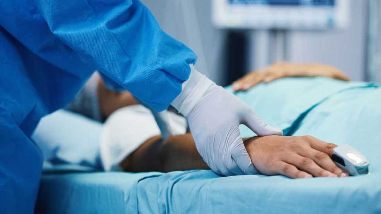 Help, healthcare and a doctor with a patient in surgery for pulse, holding hands or support. Hospital, medicine and closeup of a surgeon in theater with a person for consultation or medical nursing.