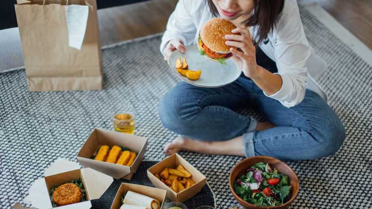 High angle view of a young woman eating takeaway food, sitting on the floor at home.