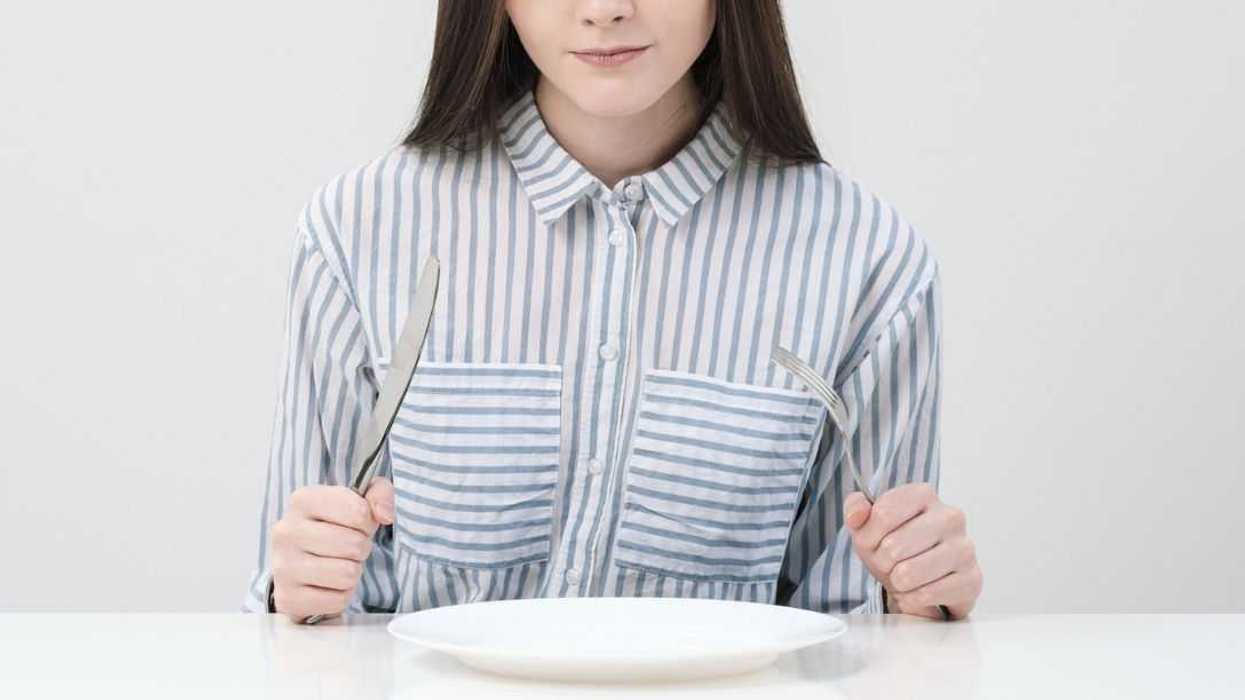 Hungry thin girl sitting at the table in front of an empty plate with a knife and fork.